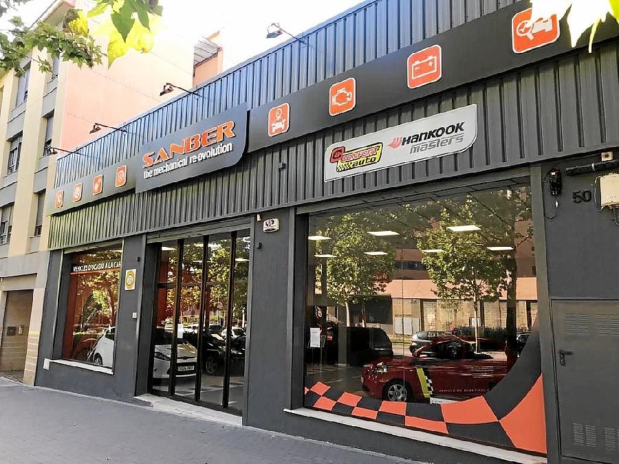 Fachada del Taller Sanber: nave gris con el letrero naranja SANBER y los iconos de servicios, en la Av. de Barcelona, 50